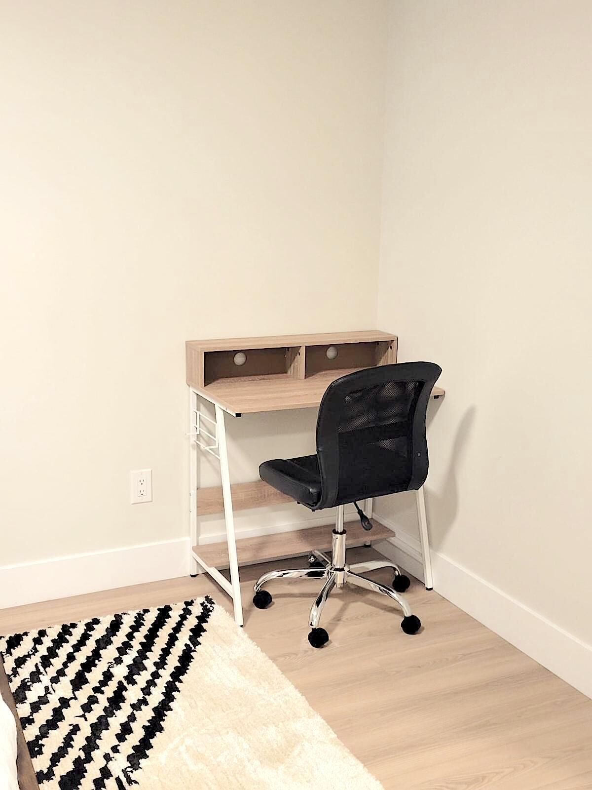 A corner office with a desk, chair, and a patterned rug.