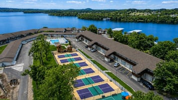 Un hotel con diversi campi da tennis, una piscina e vista su un lago.