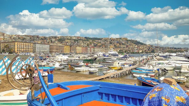 A marina with numerous boats docked, a cityscape in the background, and a clear sky.