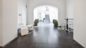 A hallway with a white door, a white bench, a small table, and a staircase leading to an upper level.