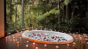 A circular hot tub surrounded by candles and rose petals, set against a backdrop of lush greenery and tall trees. - Rainforest Canopy Bungalow @ Crystal Creek Rainforest Retreat  (Upper Crystal Creek)