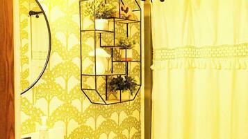 A bathroom with a toilet, a sink with a mirror, a shower curtain, and a wall-mounted shelf with plants.