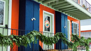 Un edifici colorit amb un balcó, una porta amb un logotip i una barana amb verdura.