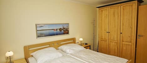 Un dormitorio con cama, mesita de noche, lámpara, armario y un cuadro en la pared.