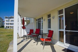 Katettu ulkotila, jossa on pöytä ja tuoleja, suuret ikkunat ja punainen aurinkovarjo.