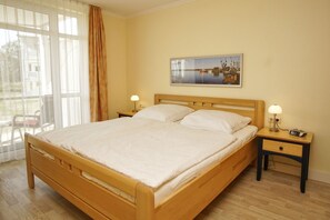 Hotellihuone, jossa on puinen sänky, kaksi yöpöytää valaisimineen, suuri ikkuna verhoineen ja taulu seinällä.