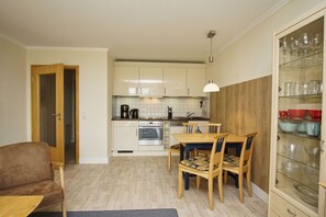 A compact kitchen with white cabinets, a dining table with chairs, and a glass cabinet with dishes.