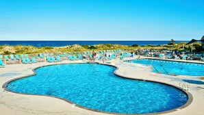 A large, kidney-shaped swimming pool with clear blue water, surrounded by lounge chairs and umbrellas, with a view of the ocean in the background. - Top of the Hill: Private Pool, Hot Tub & Sun Deck (Corolla)