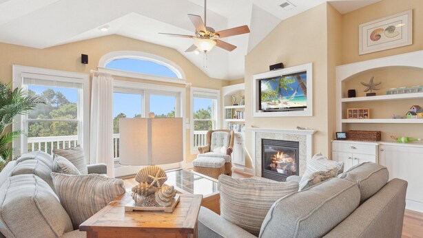 A spacious living room with a fireplace, comfortable seating, a television, and a view of the outdoors. - Top of the Hill: Private Pool, Hot Tub & Sun Deck (Corolla)