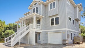 A two-story house with a covered front porch, a garage, and a staircase leading to the entrance. - Top of the Hill: Private Pool, Hot Tub & Sun Deck (Corolla)