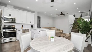 Een moderne keuken met witte kasten, een eettafel en een plafondventilator.
