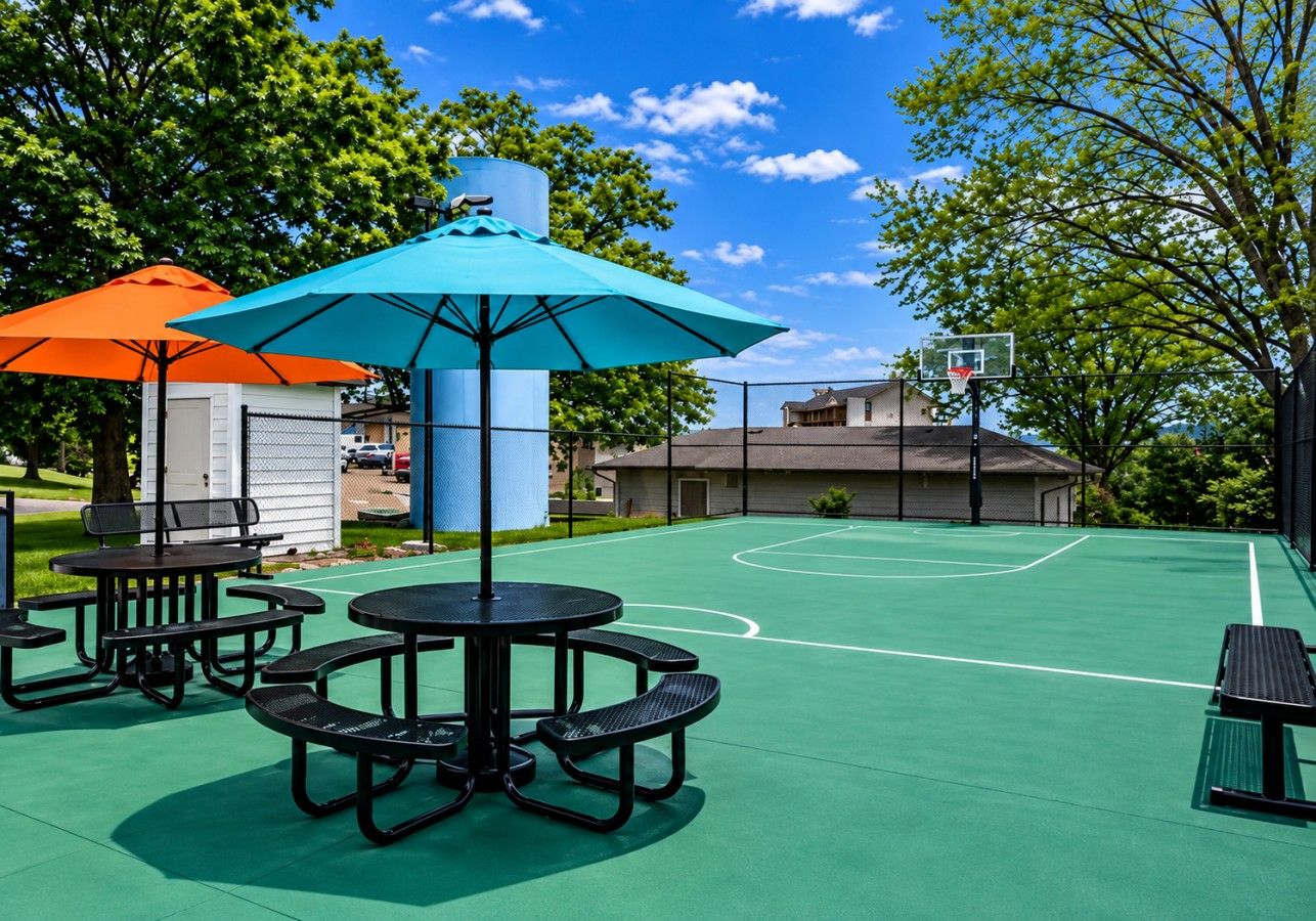 An outdoor basketball court with picnic tables and umbrellas.