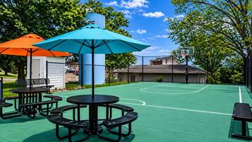 An outdoor basketball court with picnic tables and umbrellas.