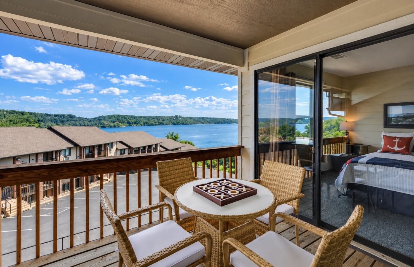 A balcony with wicker furniture, a table, and a view of a lake and buildings.