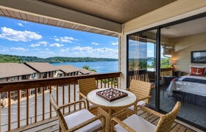 A balcony with wicker furniture, a table, and a view of a lake and buildings.