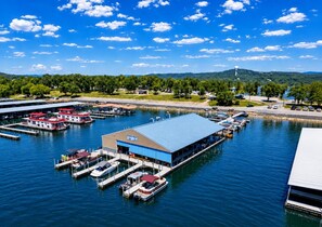 A marina with boats docked, a large building with a blue roof, and a hilly landscape in the background.
