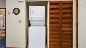 Ein Waschraum mit Waschmaschine und Trockner, Holztüren zu einem Kleiderschrank und einer wandmontierten Klimaanlage.