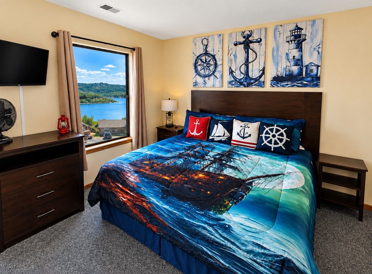 A bedroom with a large bed, a TV, a desk, and a window with a view of a lake.