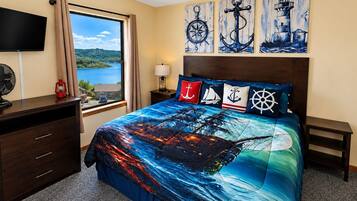 A bedroom with a large bed, a TV, a desk, and a window with a view of a lake.