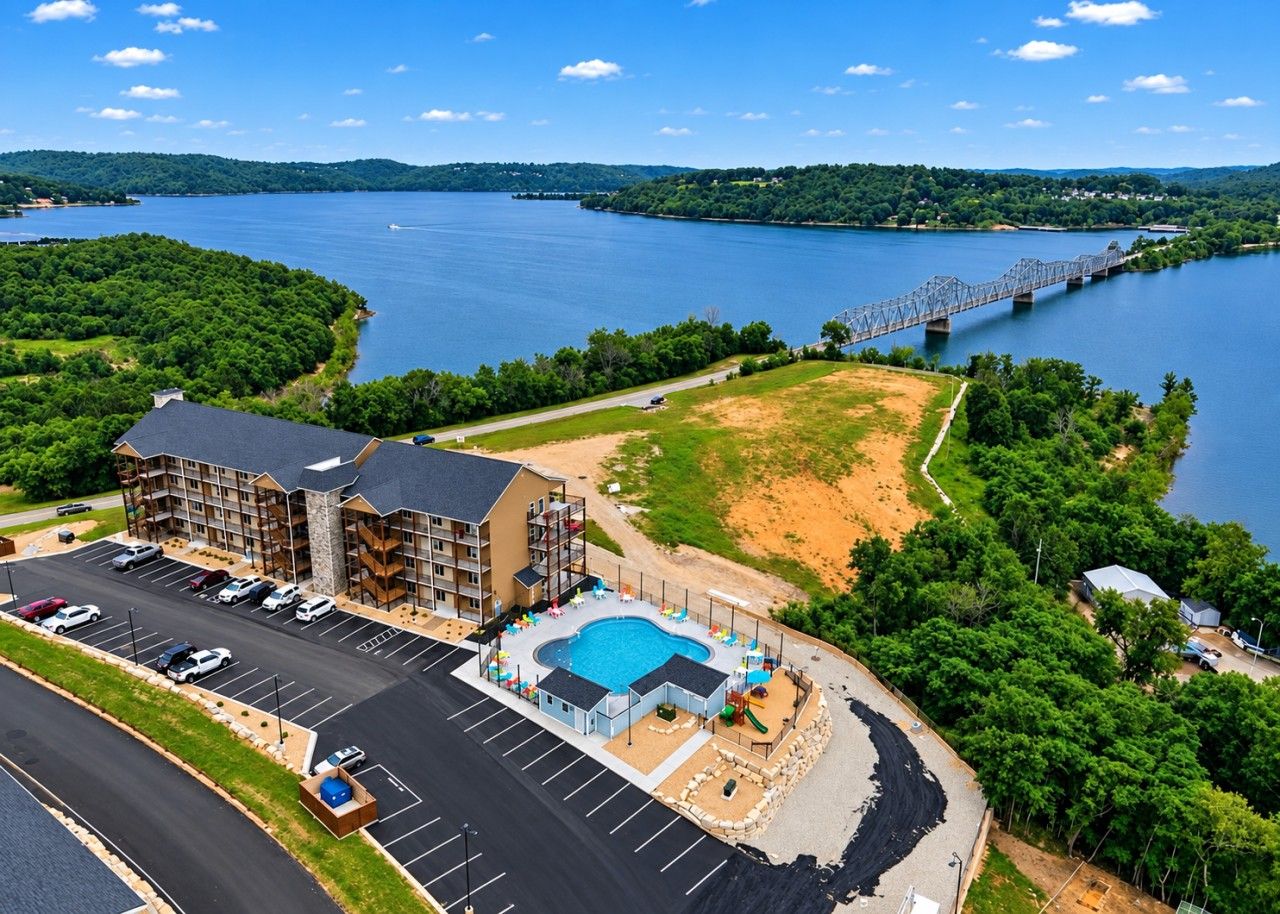 A hotel with a swimming pool, parking lot, and a view of a lake and bridge.