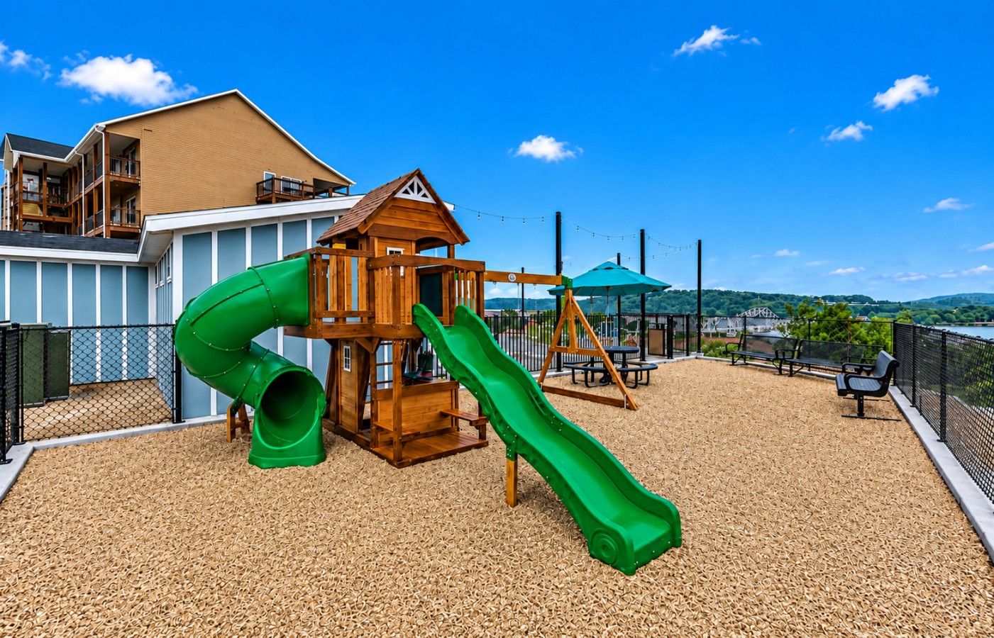 A playground with a slide and climbing structure, surrounded by a fence and a view of a body of water.