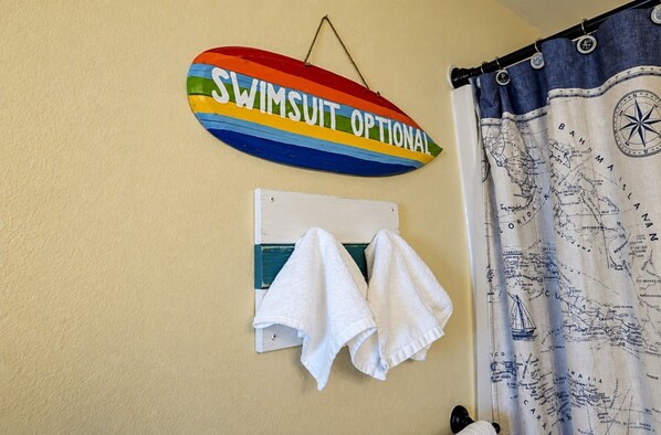 A wall-mounted sign with the text 'SWIMSUIT OPTIONAL' and a towel rack with two white towels.