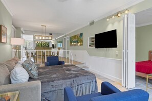 A spacious living room with a large sectional sofa, a flat-screen TV mounted on the wall, and a dining area with a high table and chairs. - Venice Beach 2 Bedroom Condo with Beach Access+Community Pool (Venice)