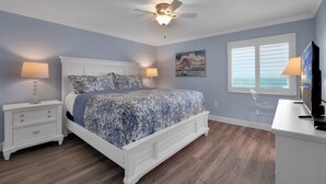 Ein Schlafzimmer mit Bett, Nachttischen, Schreibtisch, Stuhl, Deckenventilator und einem Fenster mit Jalousien.
