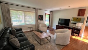 A modern living room with a black leather sofa, a white armchair, a wooden coffee table, and a flat-screen TV on a wooden cabinet. - Murfreesboro Mid-Century Modern with AC, WiFi (Murfreesboro)