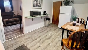 En kompakt bolig med tekøkken, spiseplads med bord og stole, sofa, lille skraldespand og køleskab.
