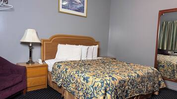 A hotel room with a bed, a nightstand with a lamp, a mirror, a purple chair, and a framed picture on the wall.