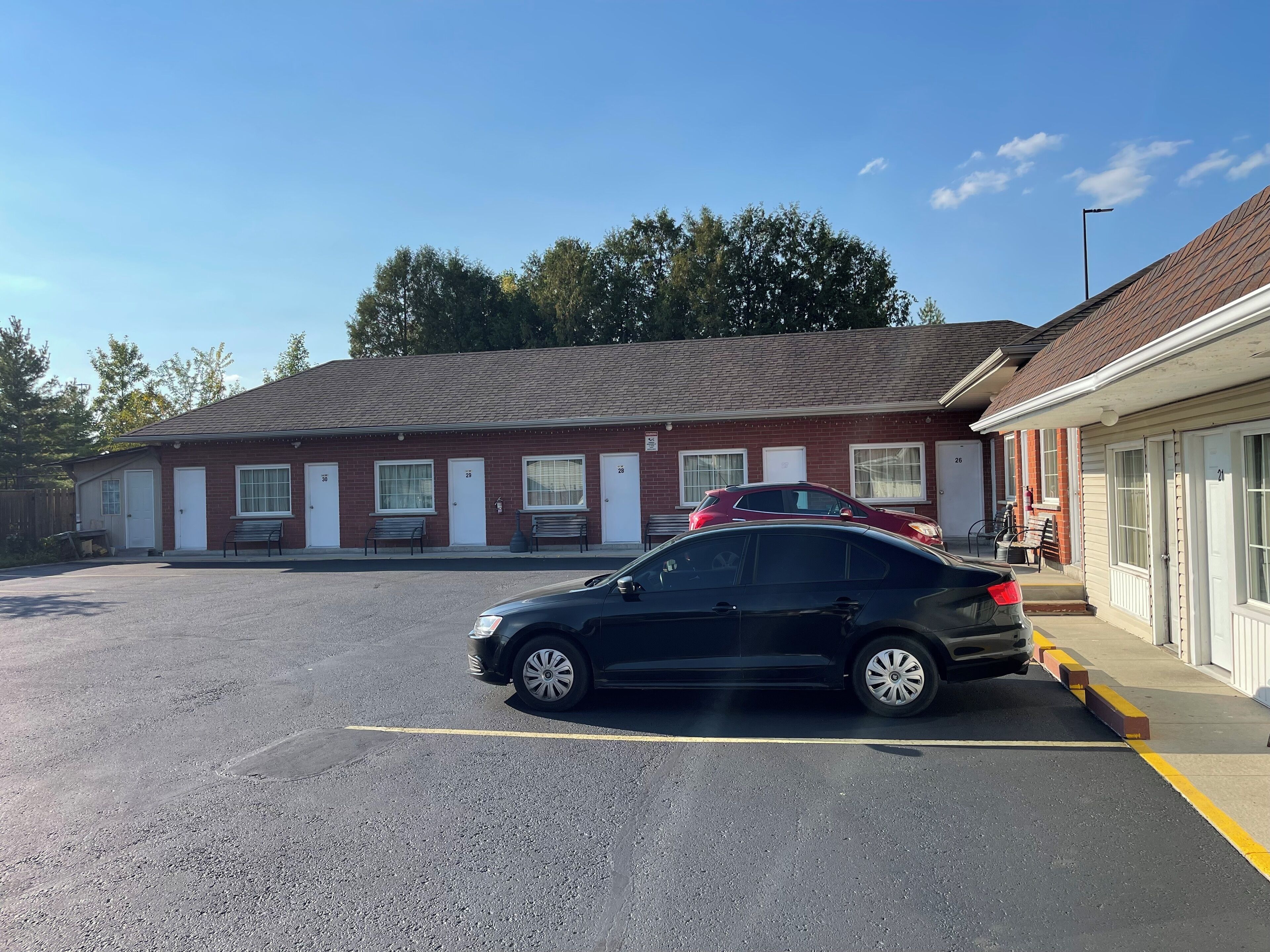 A motel with numbered rooms, a parking lot, and a red car parked in front.