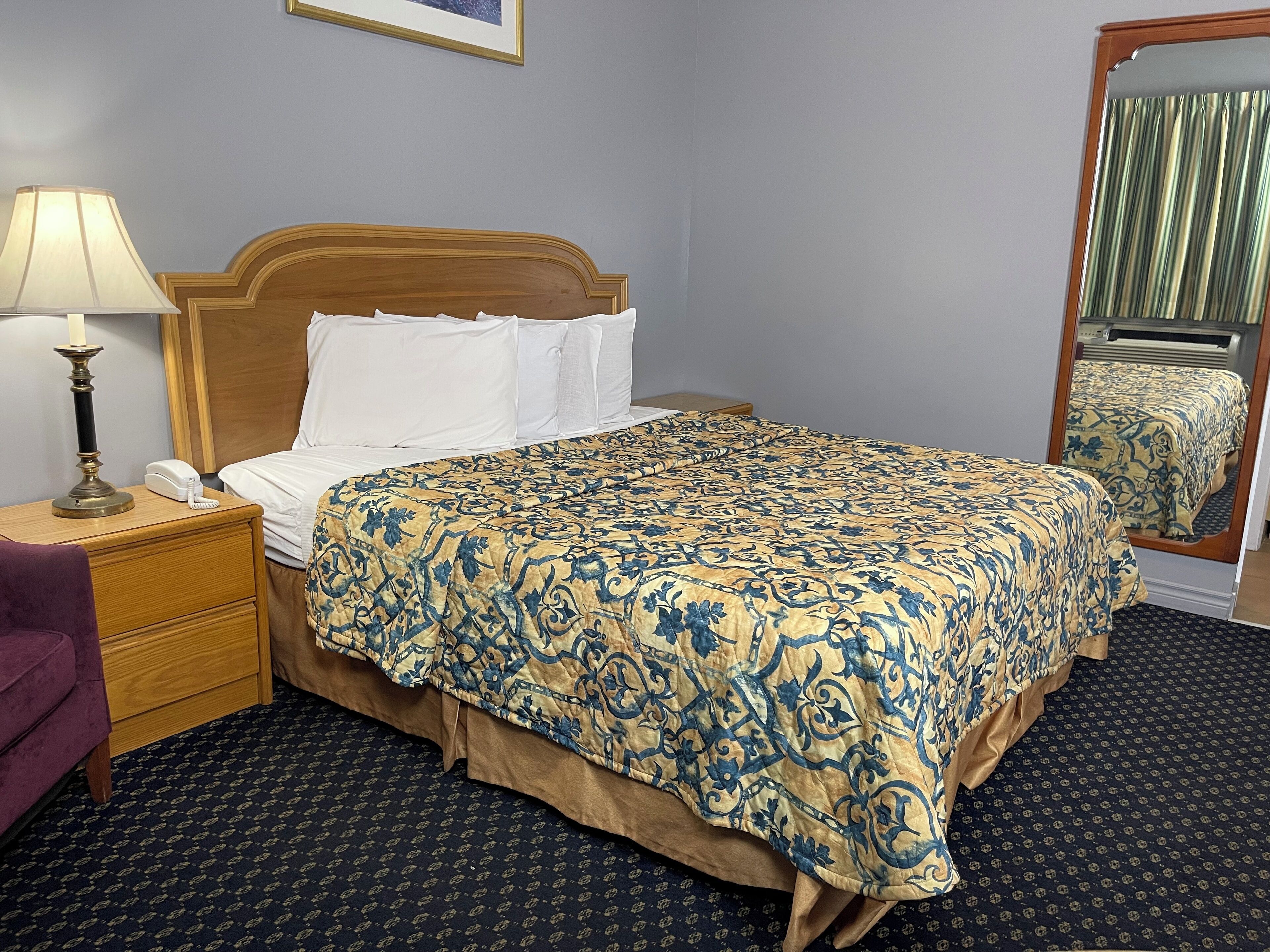 A hotel room with a bed, bedside table, lamp, phone, and a mirror.