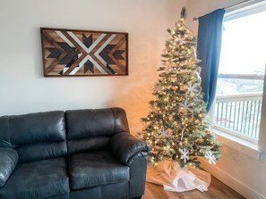 Un salon avec un canapé en cuir noir, un sapin de Noël décoré et une œuvre d’art géométrique accrochée au mur.