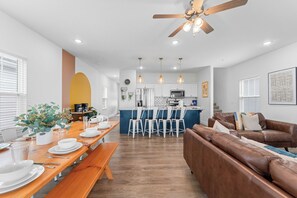 A modern living room with a brown leather sofa, a dining area with a wooden table set for four, and a kitchen in the background. - Breathtaking Lakeview Retreat with Private Hot Tub, Dog-Friendly, Cmty Pools & $400 Free Tickets (Branson)