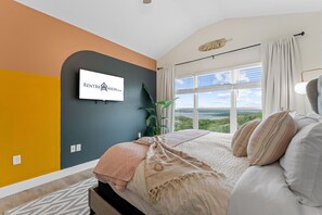Une chambre à coucher avec un lit, une grande fenêtre, une plante et un panneau accroché au mur.