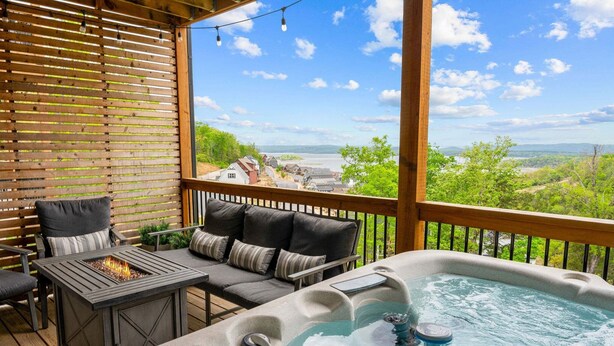 A deck with a hot tub, outdoor seating, and a view of a lake and buildings.