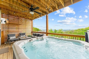 A hot tub on a wooden deck with a view of greenery and a clear sky.