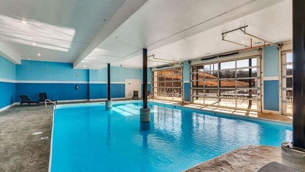 Une piscine intérieure à l’eau d’un bleu limpide, dotée d’un sol carrelé et offrant une vue sur un bâtiment extérieur grâce à de grandes fenêtres.