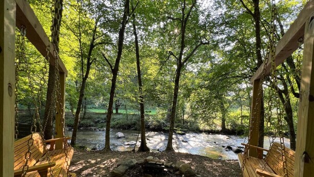 Un espace de jeux avec des balançoires en bois, donnant sur une zone boisée traversée par un ruisseau.