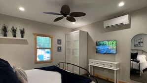 Une chambre à coucher comprenant un lit, un ventilateur de plafond, un appareil de climatisation, une télévision, une commode et une fenêtre donnant sur l’extérieur.