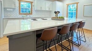 Une cuisine moderne dotée d’un grand îlot central, de tabourets de bar, de meubles blancs et d’un plancher en bois.
