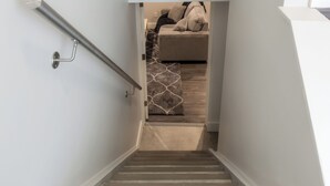 A staircase with a 'WELCOME' sign, a handrail, and a view into a room with a bed and a rug. - Fully Reno'd 2 Bedroom, 2 Bath Legal Basement Suite. Heart of the Southside (Lethbridge)