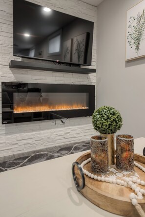 A modern living room with a fireplace, a television mounted on the wall, and a decorative tray with candles and a plant. - Fully Reno'd 2 Bedroom, 2 Bath Legal Basement Suite. Heart of the Southside (Lethbridge)