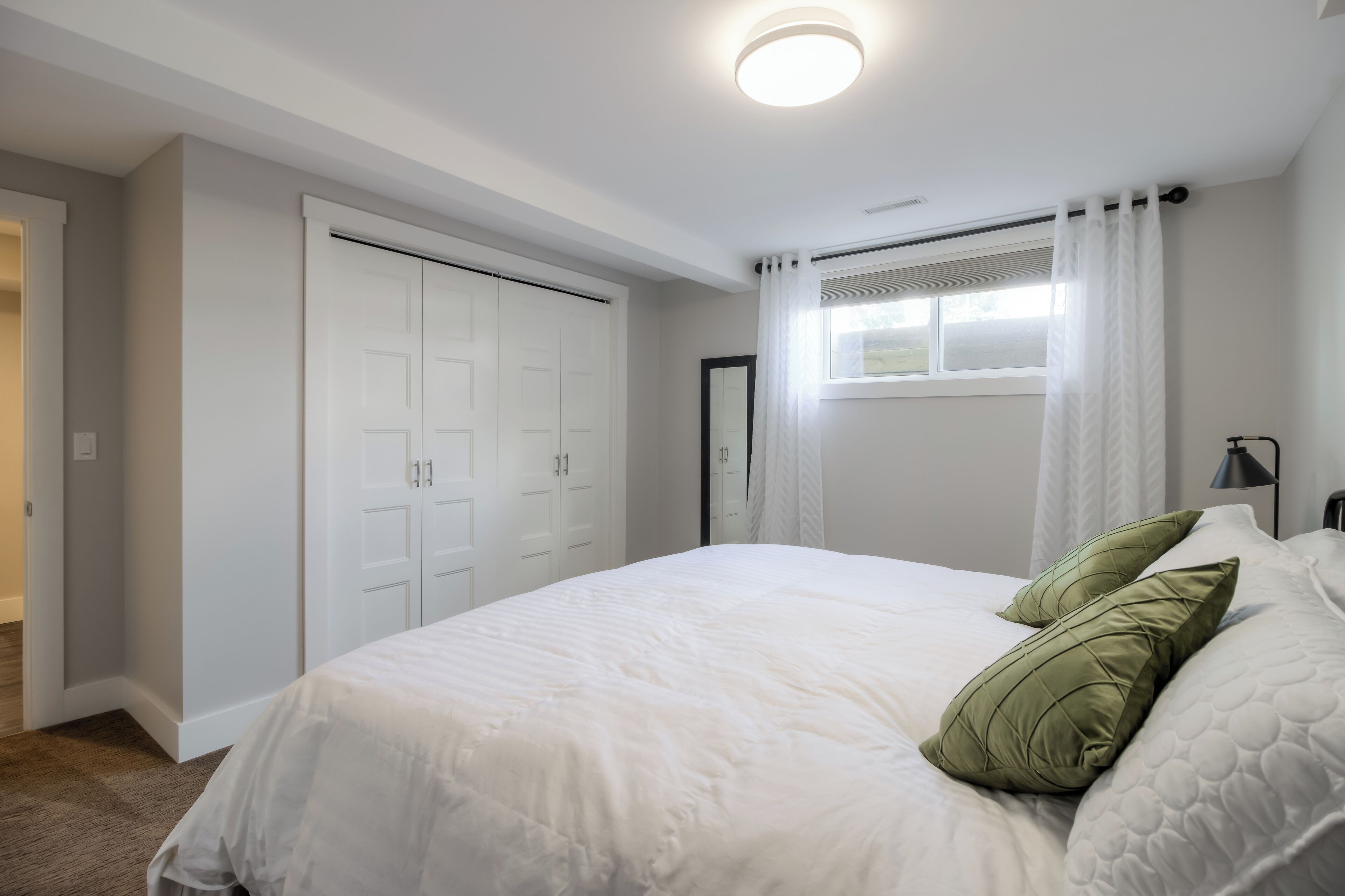 Quarto com cama, cortinas brancas, janela e porta.