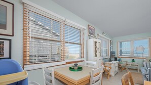 A dining area with a wooden table and chairs, a blue high chair, and a white cabinet with a television. - 7041- Duck Dog - Rodanthe Beach Cottage | Ocean Views (Rodanthe)