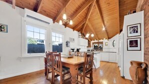 A spacious kitchen with wooden flooring, a dining table with chairs, and a high ceiling with exposed beams.