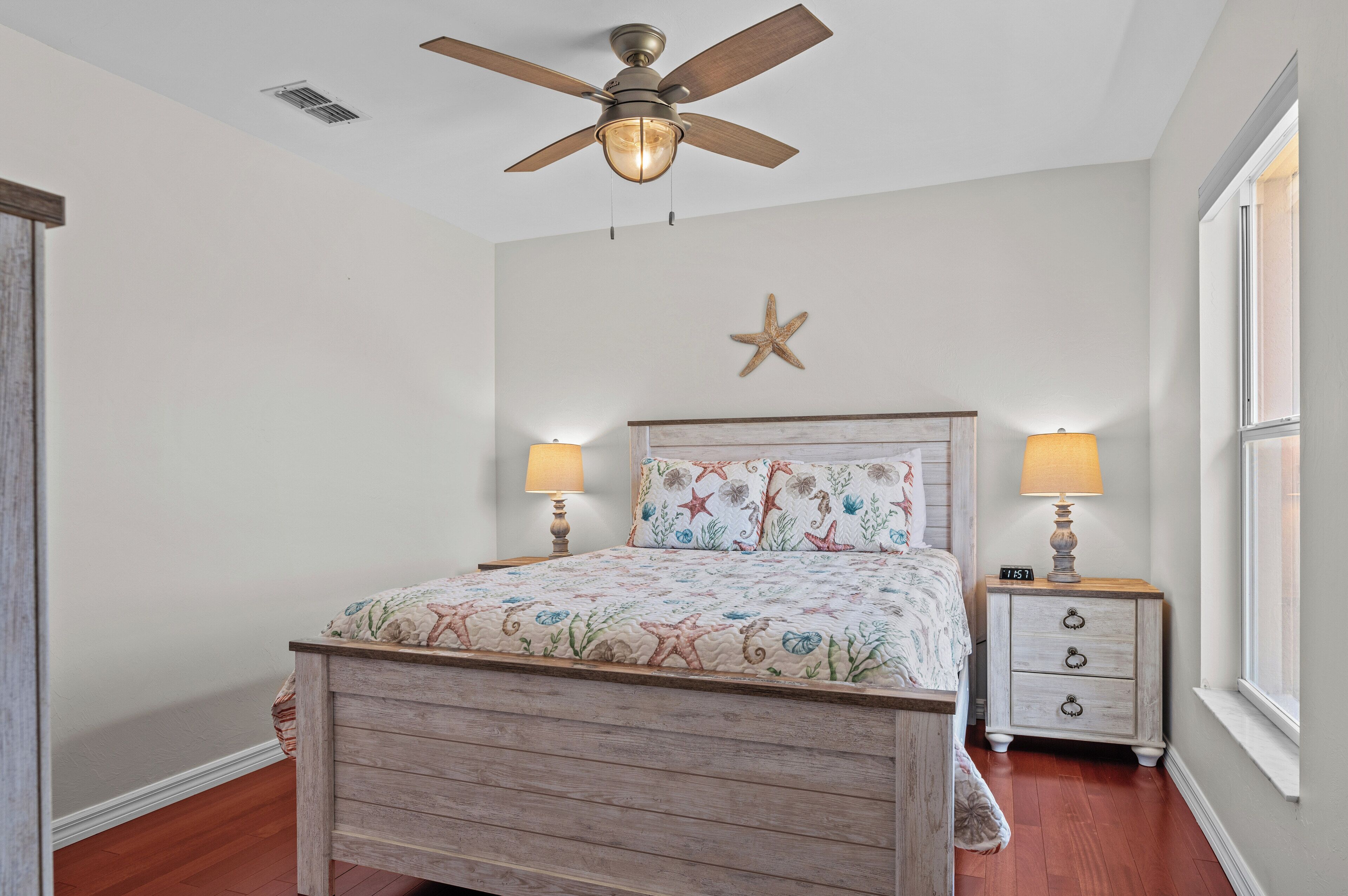 A bedroom with a wooden bed, two bedside lamps, a starfish decoration, and a ceiling fan.