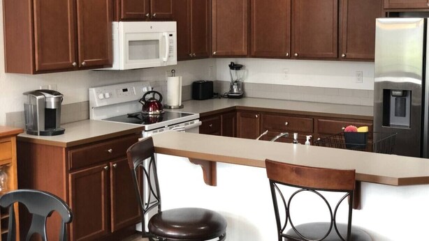 A kitchen with wooden cabinets, a white microwave, a stainless steel refrigerator, a coffee maker, and a blender.