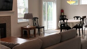 A living room with a fireplace, a sofa, a dining table with chairs, and a TV mounted on the wall.